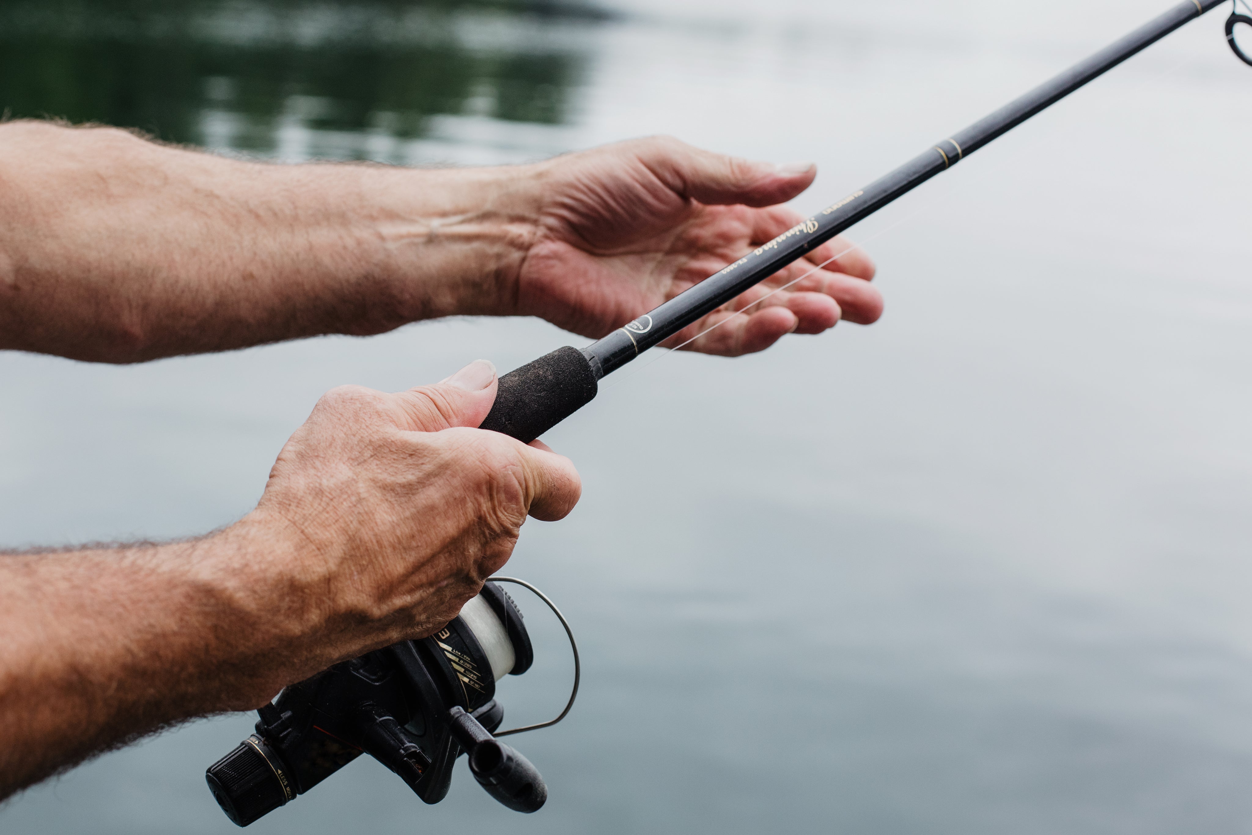 aged-hands-hold-a-fishing-rod-over-still-waters.jpg